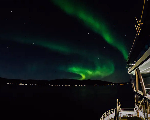 Grønt nordlys på nattehimmelen over fjell og sjø sett fra en båt