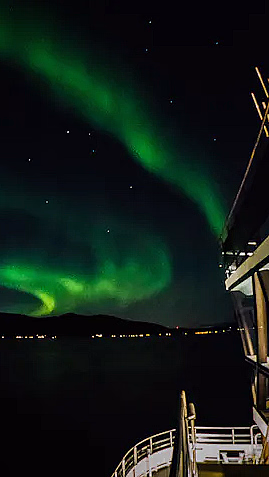 Grønt nordlys på nattehimmelen over fjell og sjø sett fra en båt