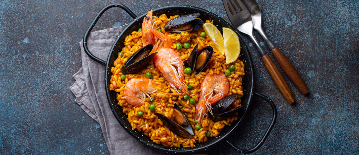 Paella med reker, blåskjell, erter og sitron i en svart panne sett ovenfra