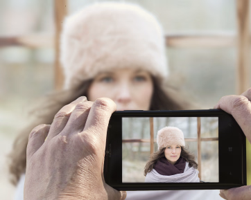 En person som tar bilde av en kvinne med pelslue og skjerf med en mobiltelefon