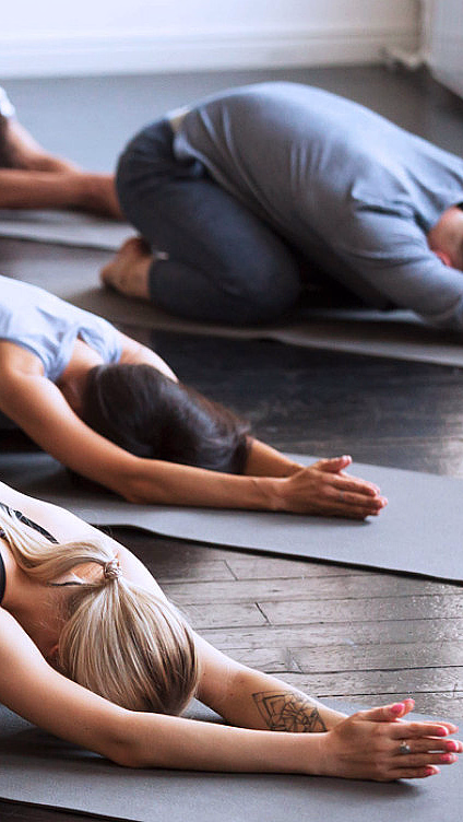 Personer i barnets posisjon på grå yogamatter på et mørkt tregulv