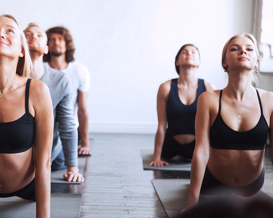 Fem personer gjør yoga på matter i et lyst rom med hvit murvegg