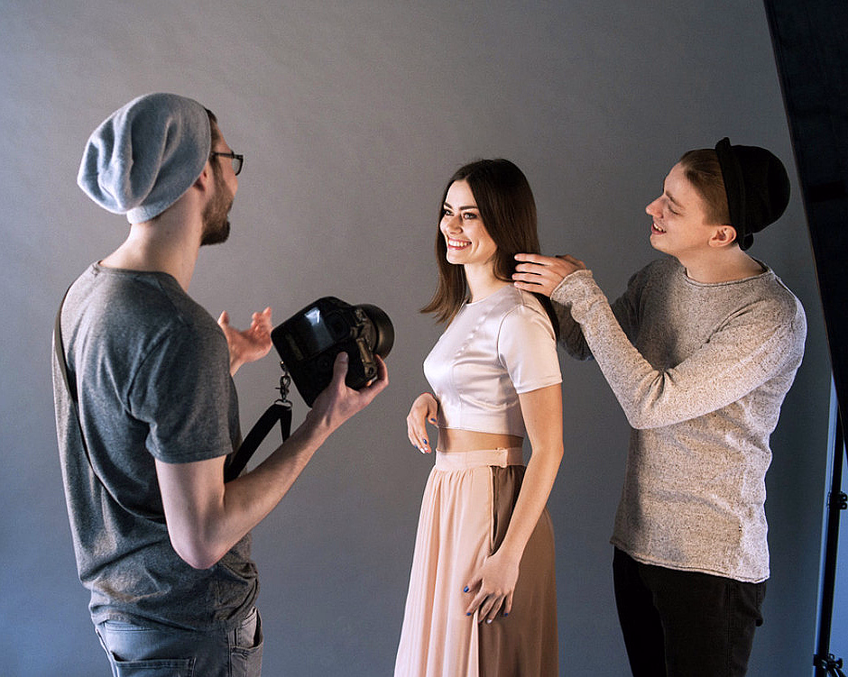 Fotograf og stylist som jobber med en smilende kvinne i et fotostudio