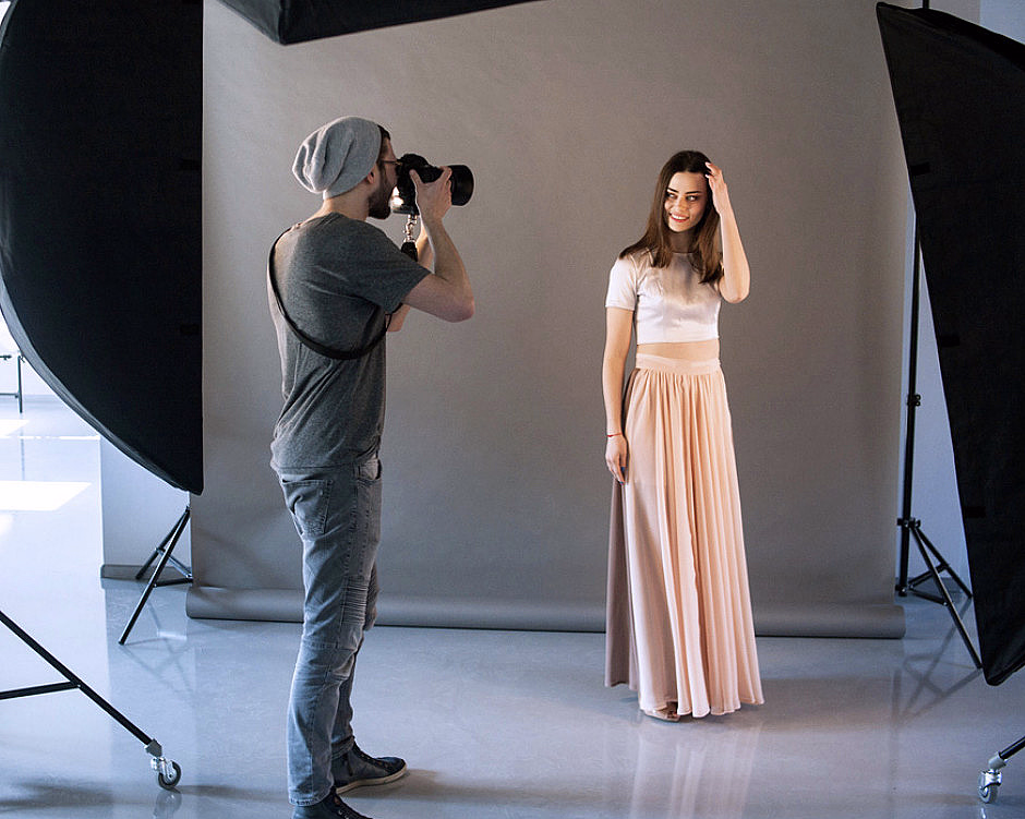 Fotograf tar bilde av en kvinne i et fotostudio med lysutstyr og grå bakgrunn