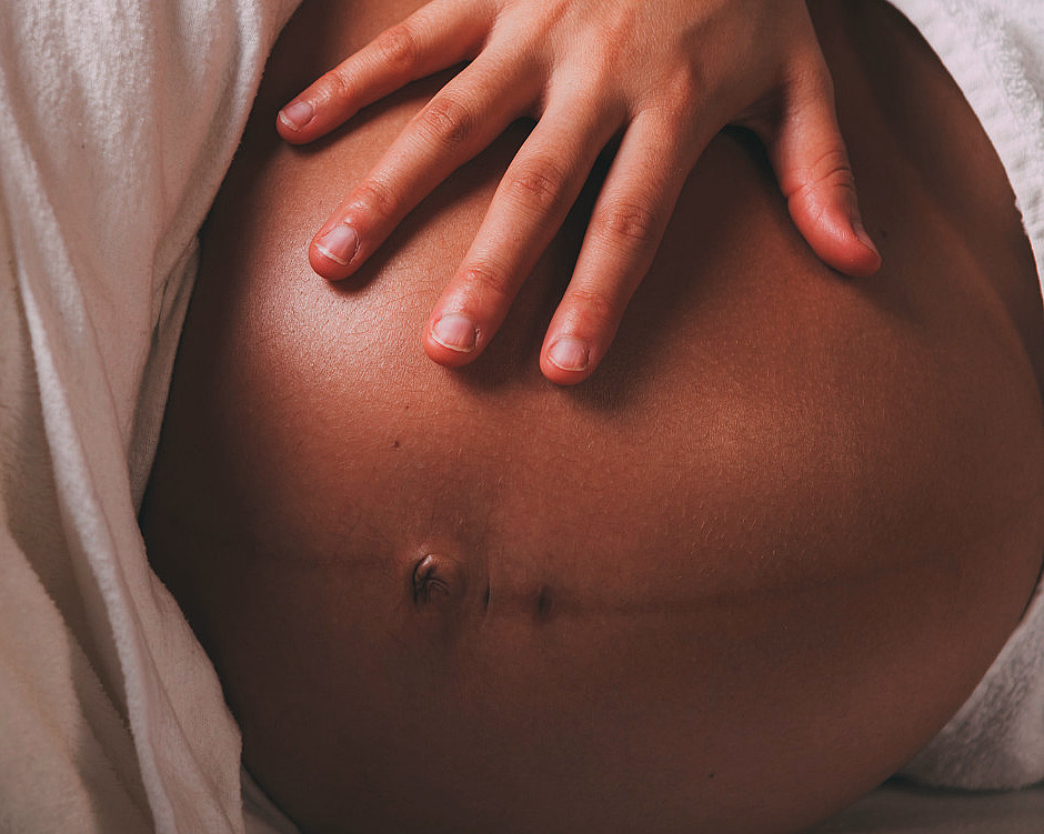 Hånd som hviler på en gravid mage delvis dekket av et lyst stoff