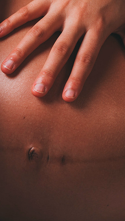 Hånd som hviler på en gravid mage delvis dekket av et lyst stoff