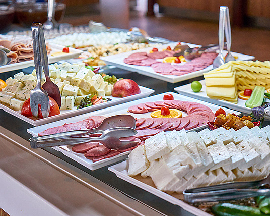 Buffet med hvite fat fylt med skivet kjøtt, ost, tomater og serveringsklyper