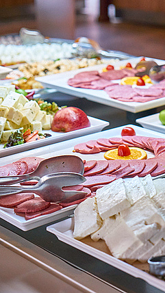 Buffet med hvite fat fylt med skivet kjøtt, ost, tomater og serveringsklyper