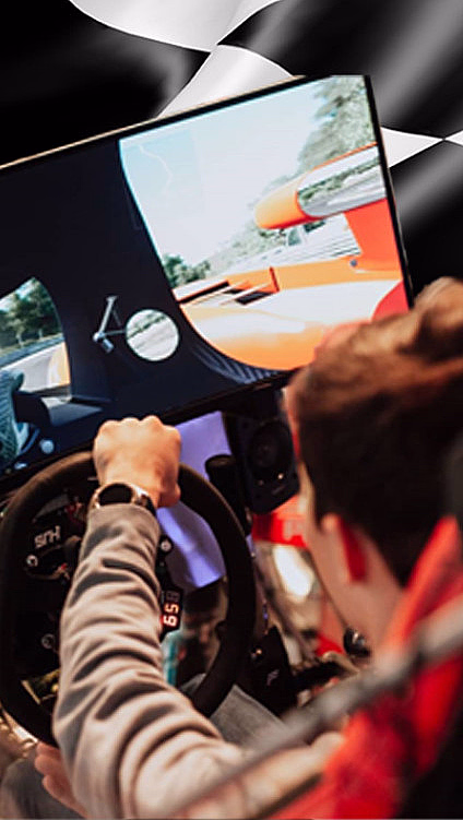 Person i en racingsimulator med ratt foran en skjerm med bilspill og rutete bakgrunn