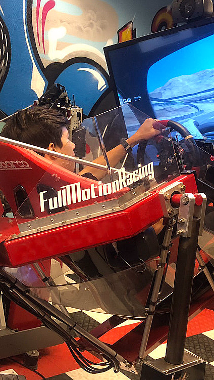 Person i rød FullMotionRacing-simulator foran skjerm med bilspill