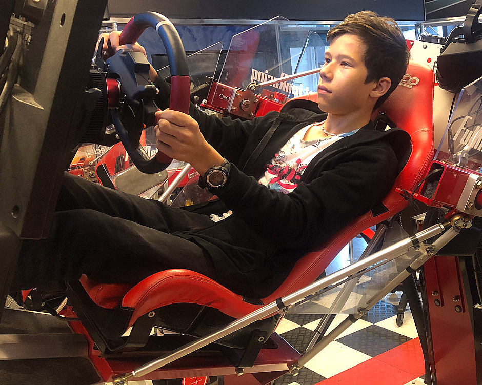 Person i et rødt racingsimulator-sete med ratt på et sjakkmønstret gulv