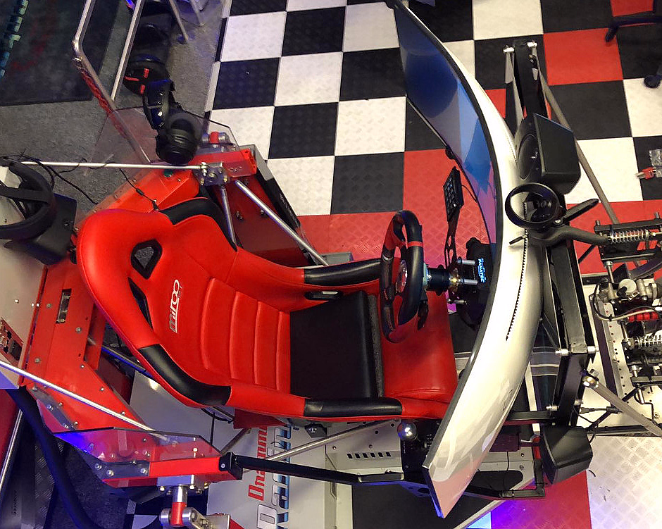 Racingsimulator med rødt sete, ratt, buet skjerm og VR-briller på rutete gulv