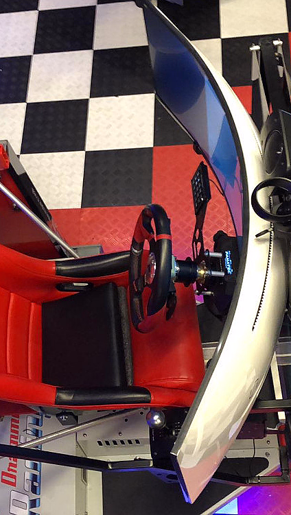 Racingsimulator med rødt sete, ratt, buet skjerm og VR-briller på rutete gulv
