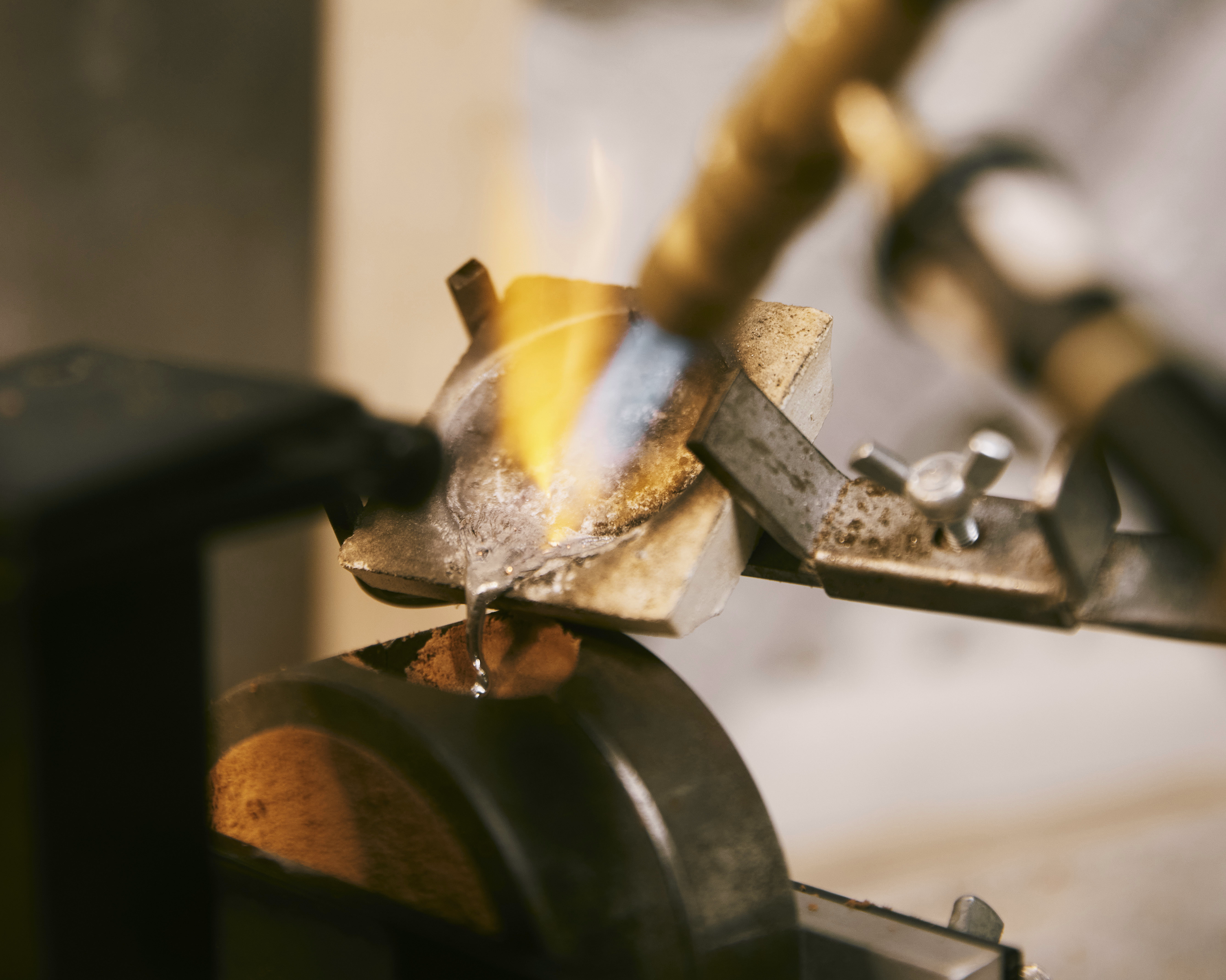Blå flamme varmer opp en liten sølvfarget gjenstand i en metallklemme