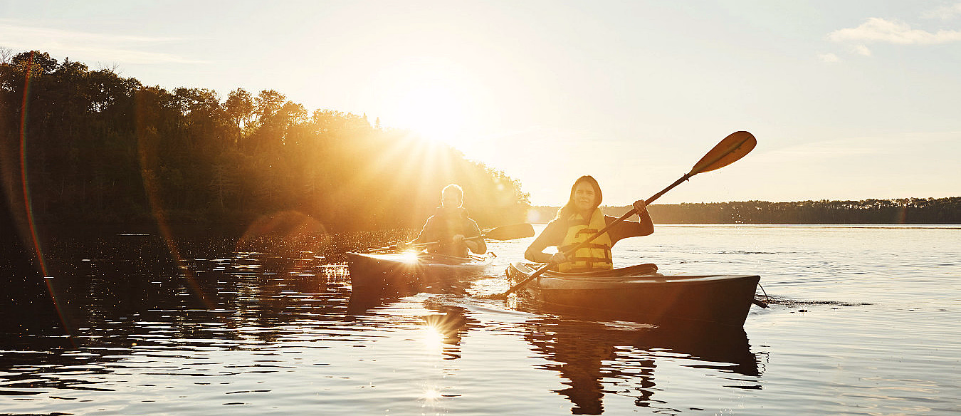 To personer padler kajakk på en innsjø i solnedgang