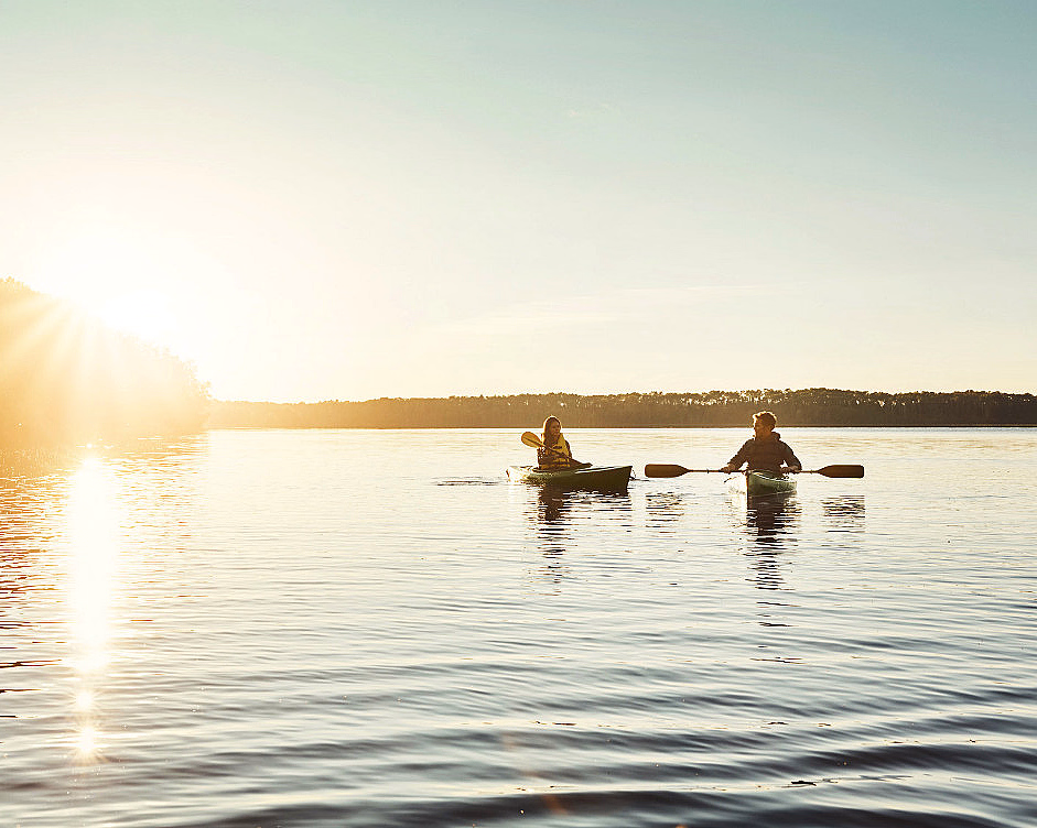 To personer padler kajakk på en rolig innsjø i solnedgang
