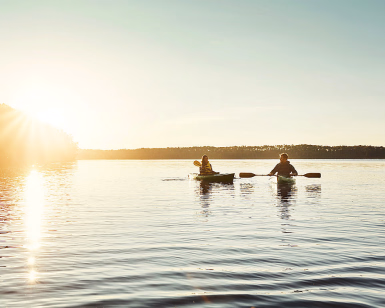 To personer padler kajakk på en rolig innsjø i solnedgang