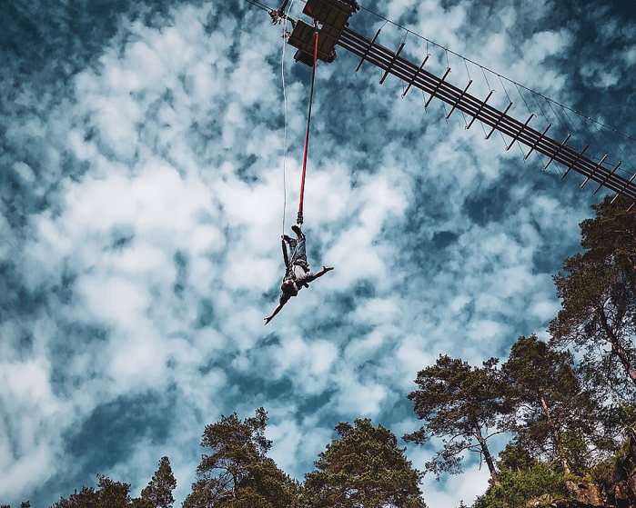 Person som hopper i strikk fra en plattform over skog og klipper
