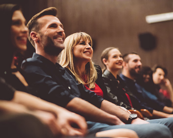 Publikum som smiler og ler i en kinosal eller et teater