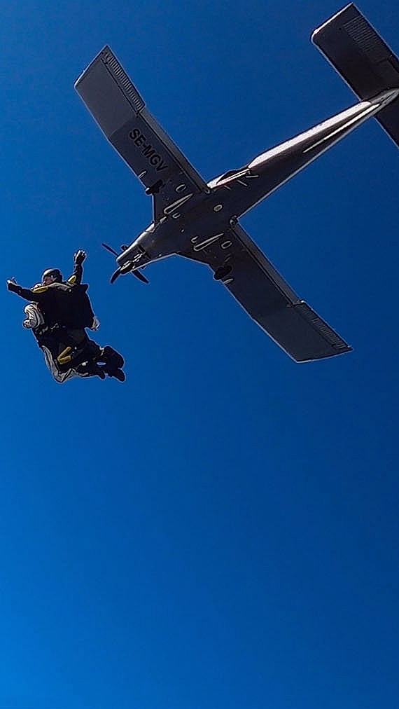 To personer i fritt fall etter å ha hoppet ut fra et fly mot en blå himmel med skyer