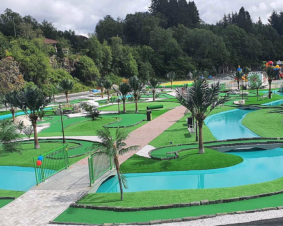 Minigolfbane med grønt kunstgress, blå vannkanaler, palmer, små broer og fargerike ballonger