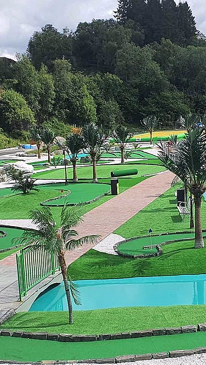 Minigolfbane med grønt kunstgress, blått vann, palmer, små broer og fargerike ballonger