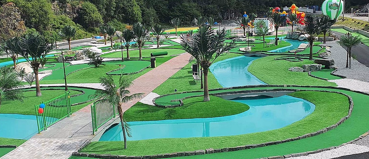 Minigolfbane med grønt kunstgress, blått vann, palmer, små broer og fargerike ballonger