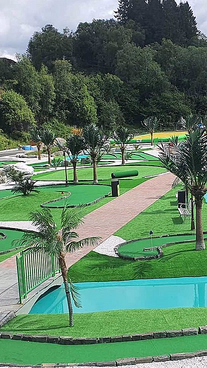 Minigolfbane med grønt kunstgress, blått vann, palmer, små broer og fargerike ballonger