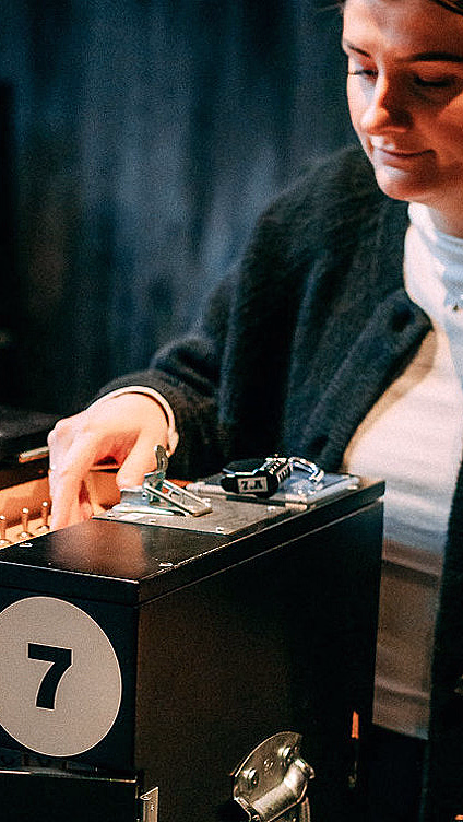 Kvinne ved en svart boks med tallet 7, ledninger og skiltet BE CREATIVE TEAM