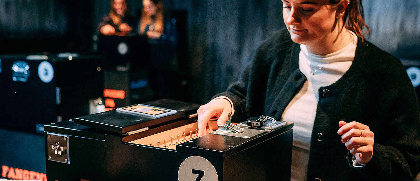 Kvinne ved en svart boks med tallet 7, ledninger og skiltet BE CREATIVE TEAM