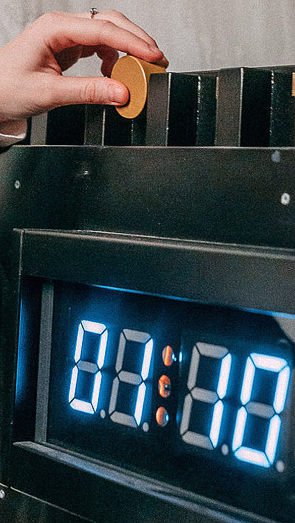 Hånd i mørk genser legger en gul polett i en svart maskin med digitalt tidsur som viser 00:00:30