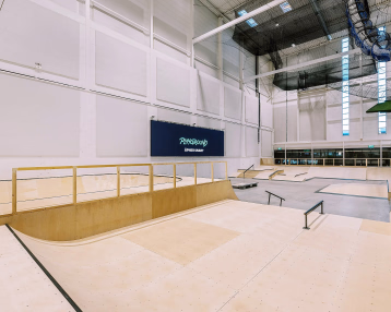Innendørs skatepark med ramper i lyst tre og et blått skilt med teksten PLAYGROUND ÅPNER SNART