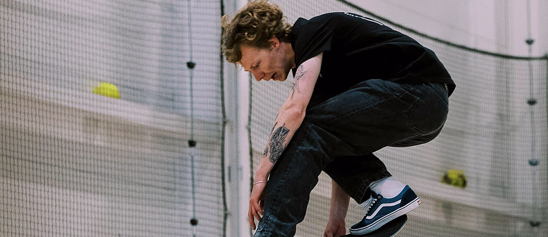 Person som gjør et hopp på skateboard i en innendørs sportshall