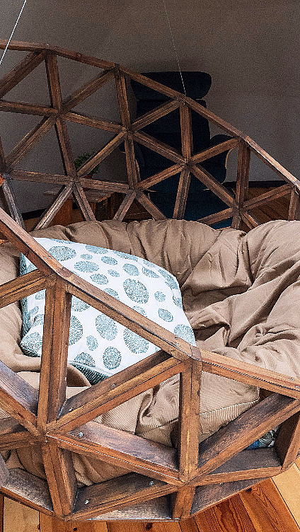 Geometrisk hengestol i tre med beige pute og blåmønstret pute i et rom med trapp