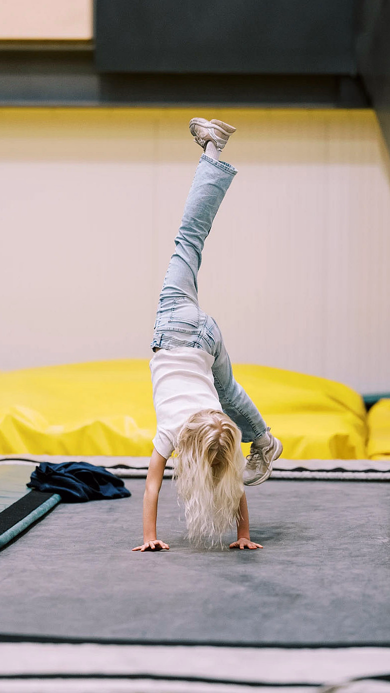 Barn med langt lyst hår gjør håndstående på en trampoline