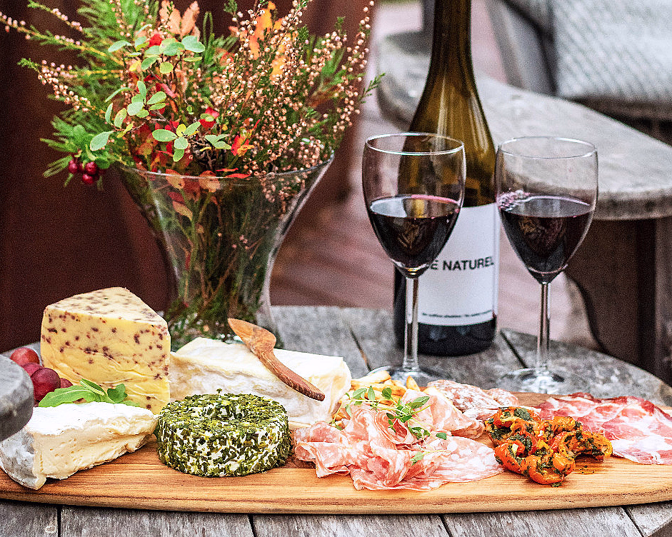 Trebrett med assorterte oster, spekemat, fylt paprika og glass med rødvin