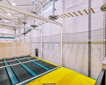 Innendørs trampolinepark med blå trampoliner, gul polstring og klatreløype
