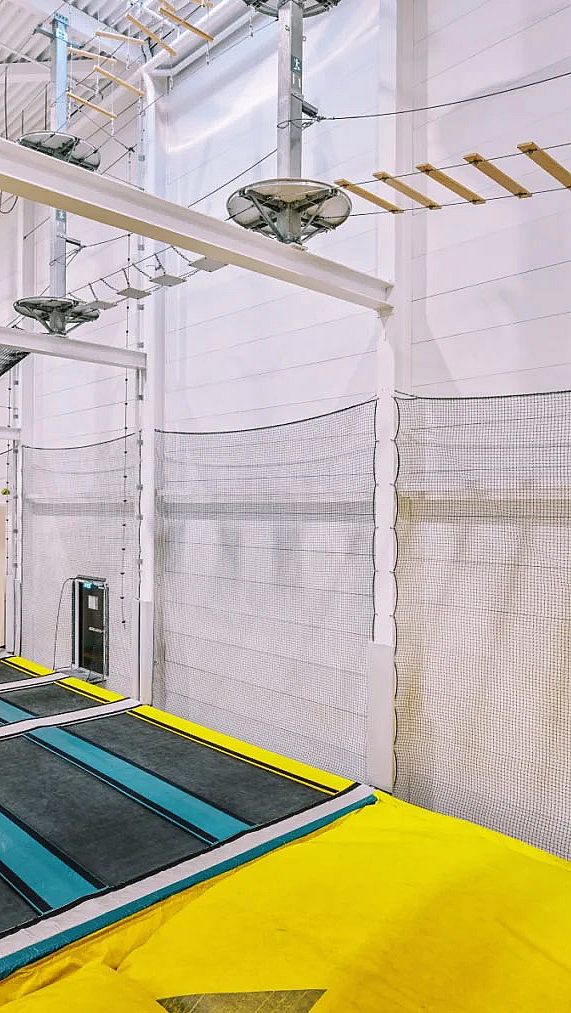 Innendørs trampolinepark med blå trampoliner, gul polstring og klatreløype