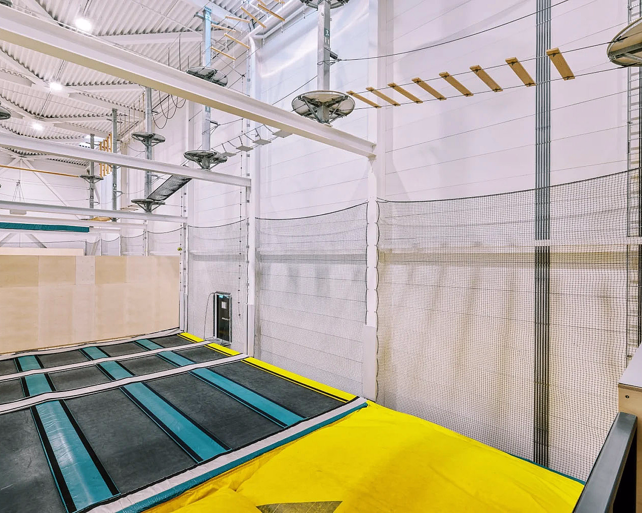 Innendørs trampolinepark med blå trampoliner, gul polstring og en klatreløype over
