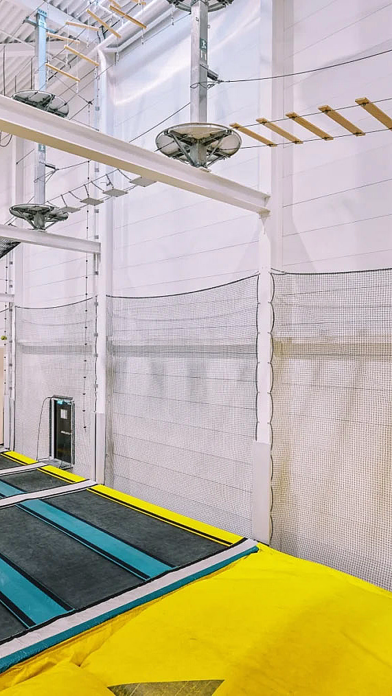 Innendørs trampolinepark med blå trampoliner, gul polstring og en klatreløype over