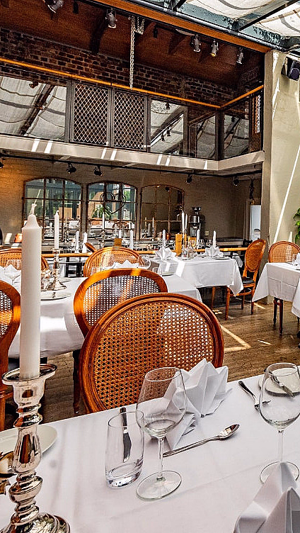 Lyst restaurantlokale med hvite duker og trestoler ved store vinduer med hageutsikt