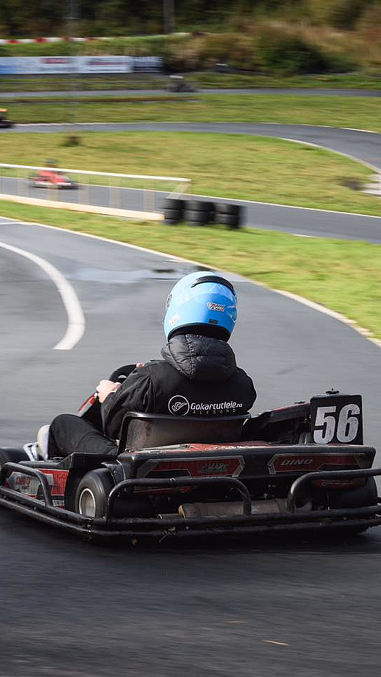 Person i blå hjelm kjører gokart nummer 56 på en svingete asfaltbane med et gult SLOW-skilt
