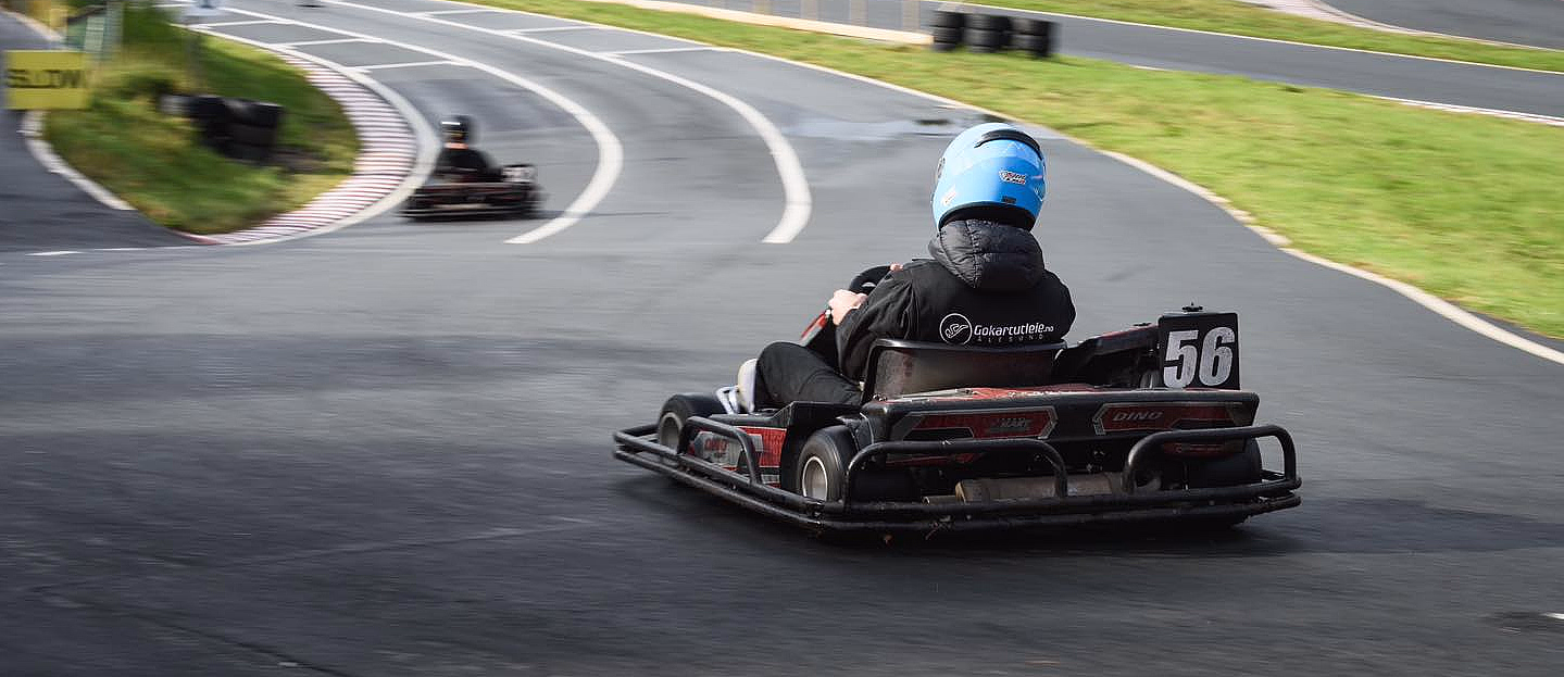 Person i blå hjelm kjører gokart nummer 56 på en svingete asfaltbane med et gult SLOW-skilt