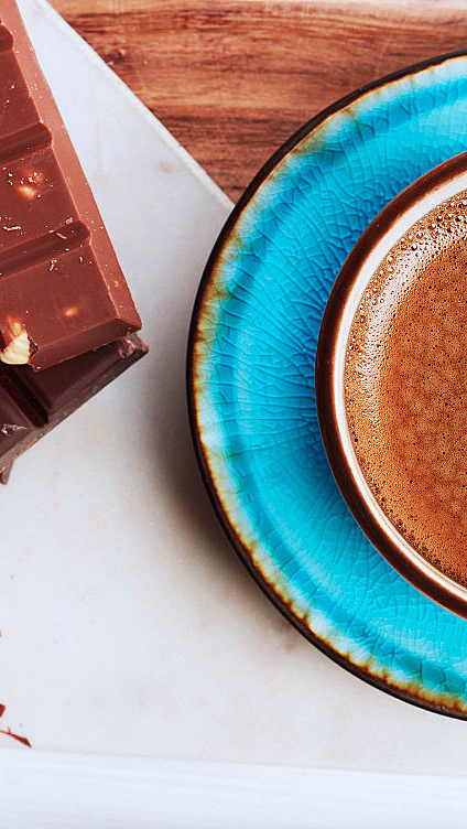 Kaffekopp på blått tefat ved siden av sjokoladeplater med nøtter og kakaobønner