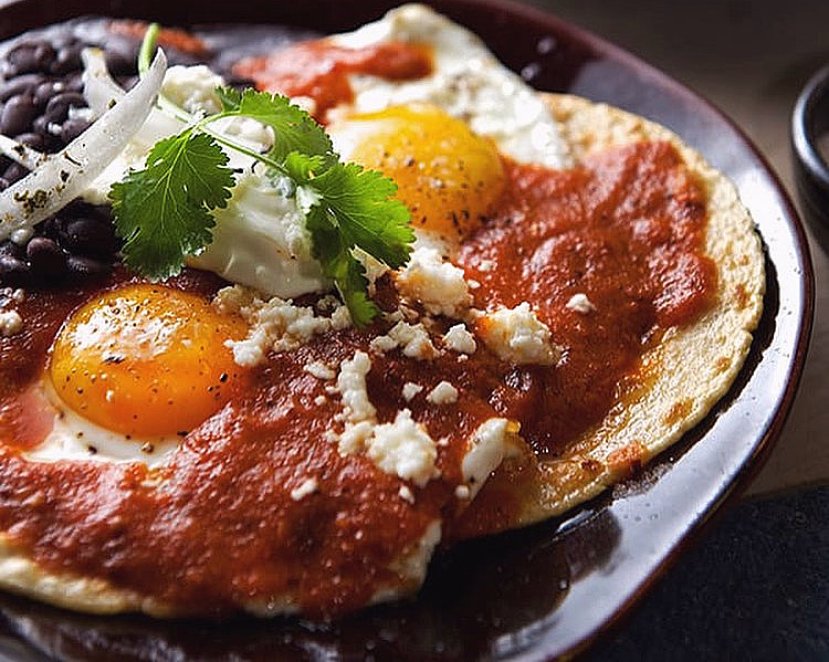 To tallerkener med tortilla, speilegg, rød salsa, svarte bønner, hvit ost og koriander