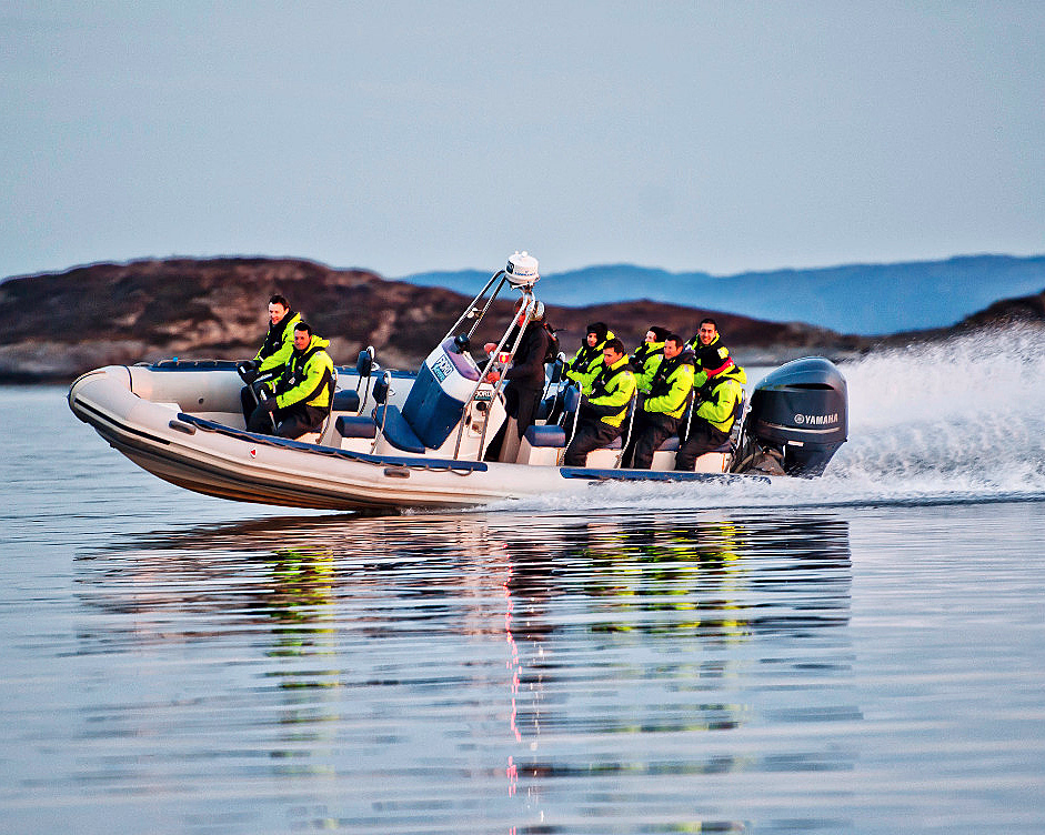 Personer i gule jakker på en hurtiggående rib-båt på blikkstille vann
