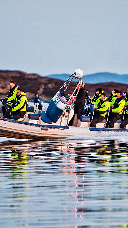 Personer i gule jakker på en hurtiggående rib-båt på blikkstille vann