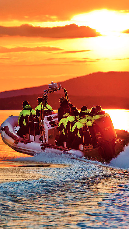 Hurtiggående båt med folk i gule redningsvester på vannet i solnedgang
