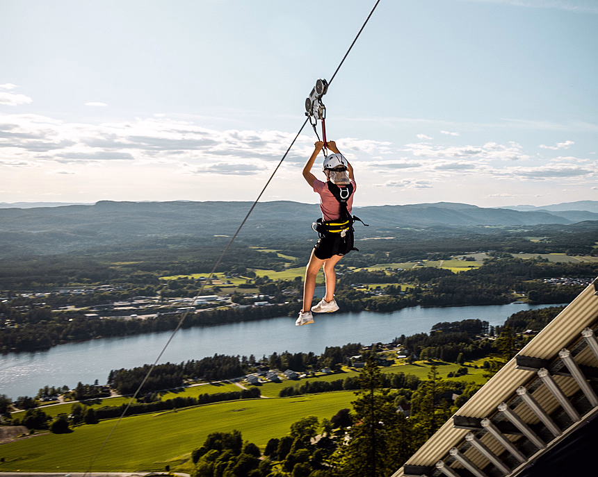 Person i zipline over en elv og et grønt landskap med fjell i bakgrunnen