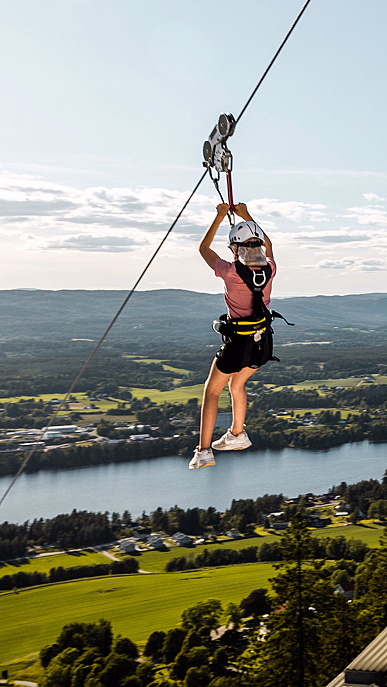 Person i zipline over en elv og et grønt landskap med fjell i bakgrunnen